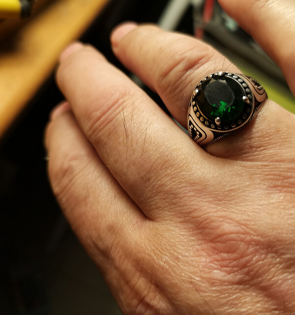 Close-up of a hand wearing a ring with a green gemstone.