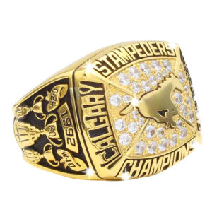 Close-up of a gold championship ring with 'Stampeders' and 'Calgary Champions' inscriptions.